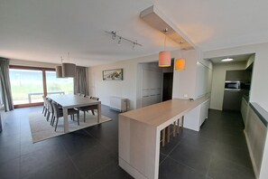 Eine moderne Küche mit einer zentralen Kochinsel, einem Essbereich mit Tisch und Stühlen und Blick durch die Glastür.