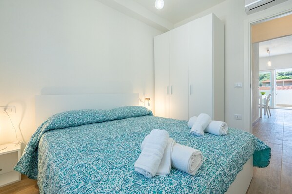 A bedroom with a bed, two white cabinets, a small table, and a door leading to an outdoor area.