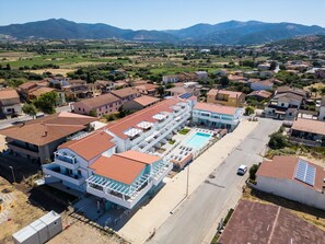 A modern hotel with a swimming pool, multiple floors, and a view of surrounding residential area and mountains. - Affittimoderni Santa Maria Coghinas - Casa Fiore (Santa Maria Coghinas)