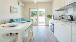 Eine moderne Küche mit weißen Schränken, eine Essecke mit einem weißen Tisch und Stühlen sowie eine Glastür, die zu einem Außenbereich führt.