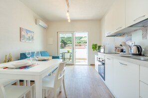 Eine moderne Küche mit weißen Schränken, eine Essecke mit einem weißen Tisch und Stühlen sowie eine Glastür, die zu einem Außenbereich führt.