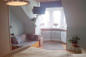 A bedroom with a bed, a sofa, a TV, a window, and a radiator. - Holiday apartment with 1 bedroom (Weißenstadt)