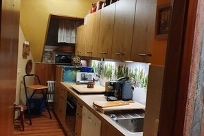 A compact kitchen with wooden cabinets, a coffee maker, a toaster, and a small dining area with a chair and table. - Holiday apartment with 1 bedroom (Weißenstadt)