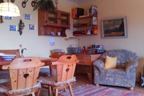 A cozy living room with a wooden dining table, chairs, a patterned armchair, a bookshelf, and a painting on the wall. - Holiday apartment with 1 bedroom (Weißenstadt)
