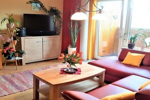 A living room with a sofa, a coffee table, a TV, and potted plants. - Holiday apartment with 1 bedroom (Weißenstadt)