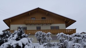 Ein zweistöckiges Gebäude mit einem Holzbalkon, schneebedeckten Bäumen und einem geneigten Dach.