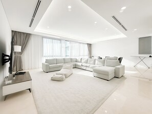 A modern living room with a sectional sofa, a flat-screen TV mounted on the wall, a coffee table, and a floor lamp. - D'Rapport Residences By Manhattan Plus (Ampang)