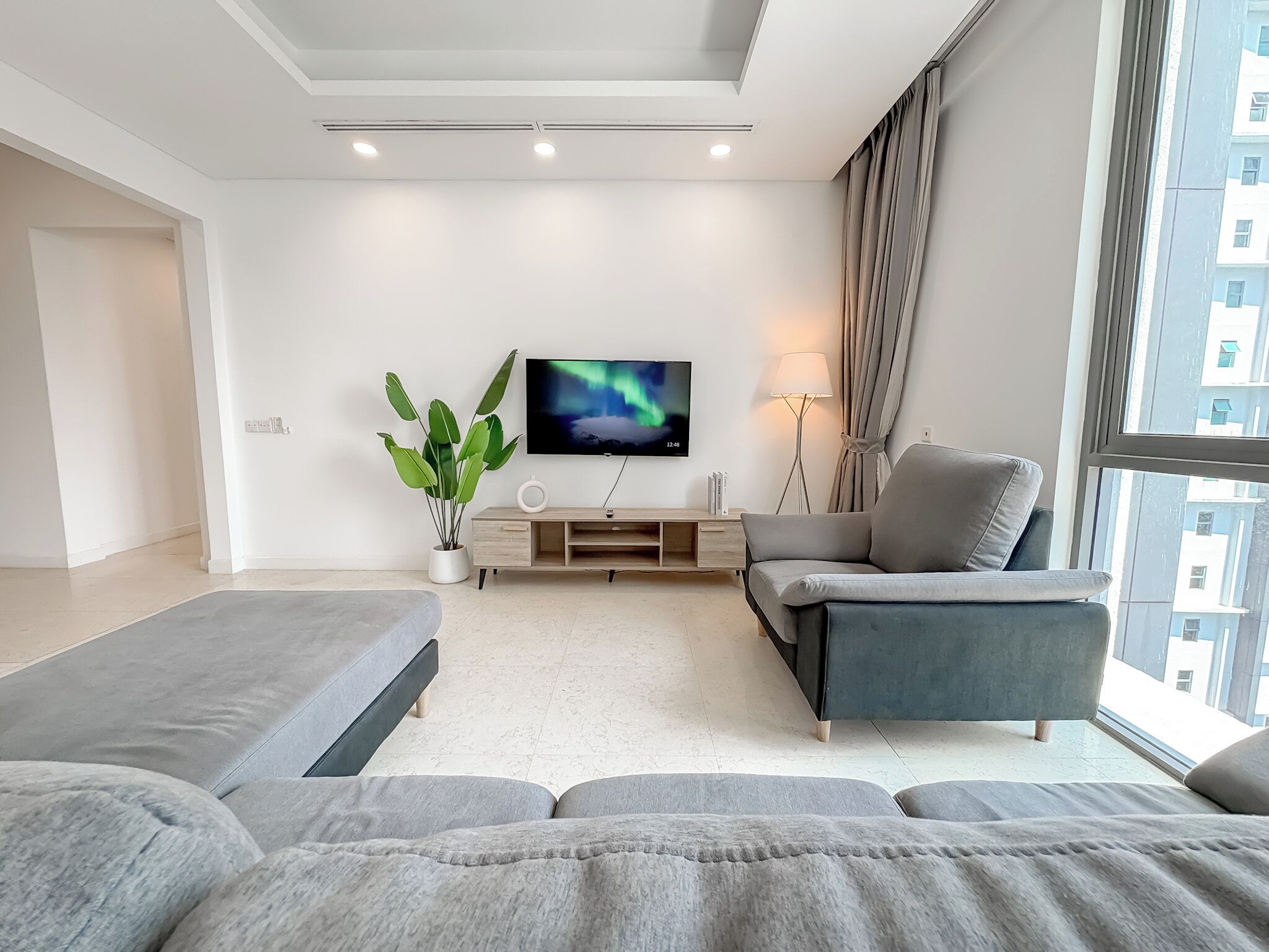 A modern living room with a flat-screen TV, a potted plant, a sofa, a chair, and a lamp.