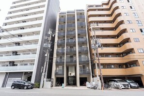 A multi-story building with balconies, a covered entrance, and parked vehicles. - T-FLAT NAMBA WEST (Sakuragawa, Naniwa)