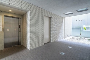 A modern building exterior with a brick wall, a glass entrance, and an elevator. - T-FLAT NAMBA WEST (Sakuragawa, Naniwa)