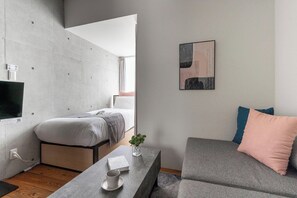 Ein modernes Zimmer mit einem Bett, einem Sofa, einem Couchtisch, einem Fernseher und einem Bild an der Wand.