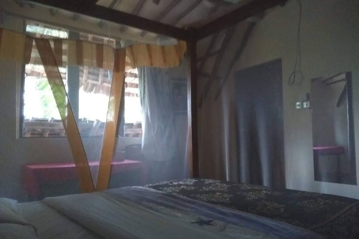 Una habitación con una cama, una ventana con cortinas, una puerta y una mesita.