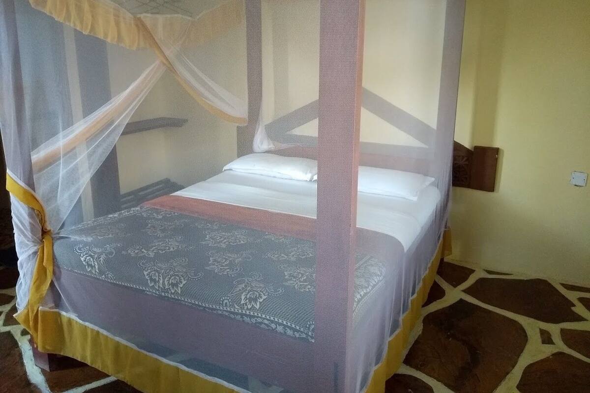 Una cama con dosel y cuatro columnas, una colcha estampada y un suelo de baldosas.