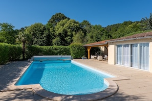A swimming pool with a sunken area, a covered patio with outdoor furniture, and a building with large windows.