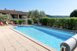 A swimming pool with lounge chairs, a house, and a view of hills.