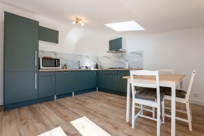 A modern kitchen with teal cabinets, a microwave, and a dining area with a wooden table and chairs. - Villa "De L’Olivier" with Private Pool, Wi-Fi, and Air Conditioning (Labégude)