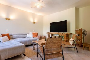 Una sala de estar con un sofá modular, un televisor de pantalla plana, sillas de mimbre y una mesa de centro de madera.