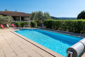 A swimming pool with a tiled deck, a house in the background, and a clear sky.