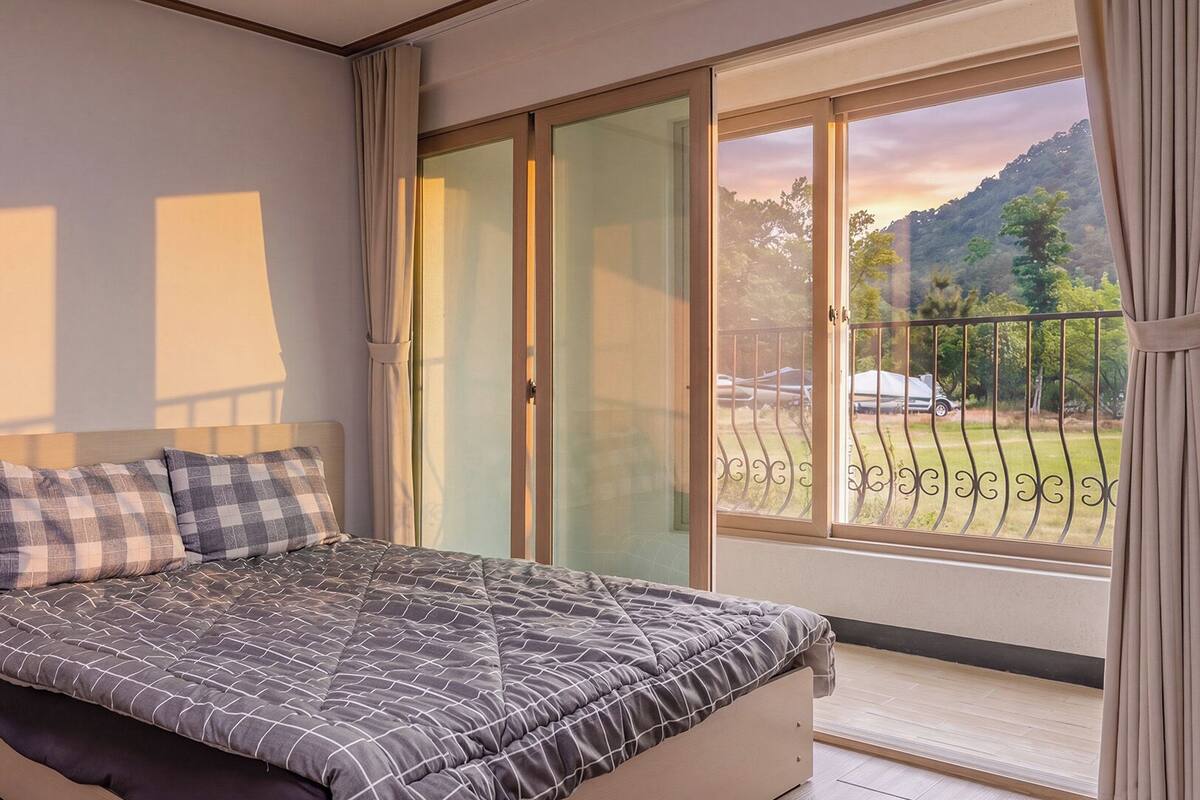 Un dormitorio con cama, ventana con vista al exterior y balcón con barandilla.