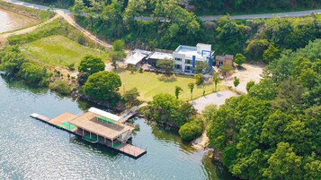 Vista aérea de una propiedad junto al lago con un muelle, una casa grande y vegetación circundante.