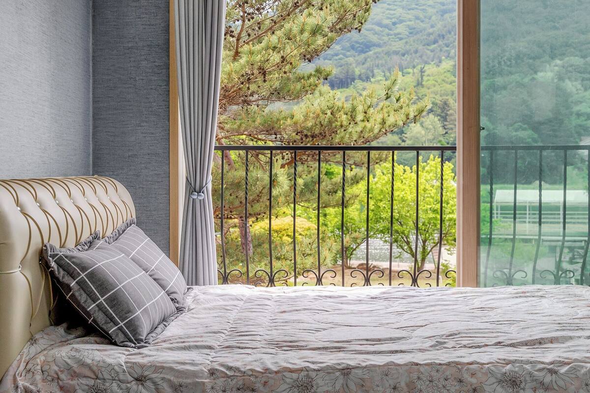 Un dormitorio con cama, vistas a árboles y un lago, y un balcón con barandilla.