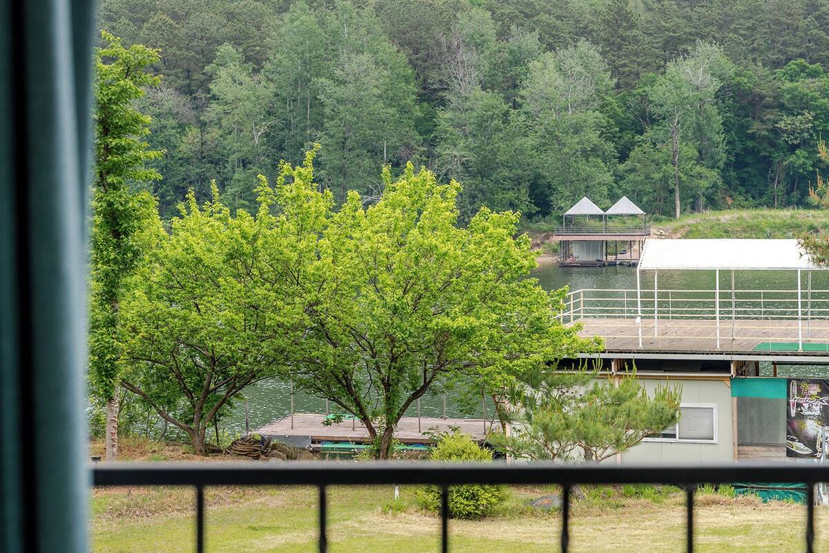 Vista de un lago con un muelle, árboles y un edificio con techo verde.