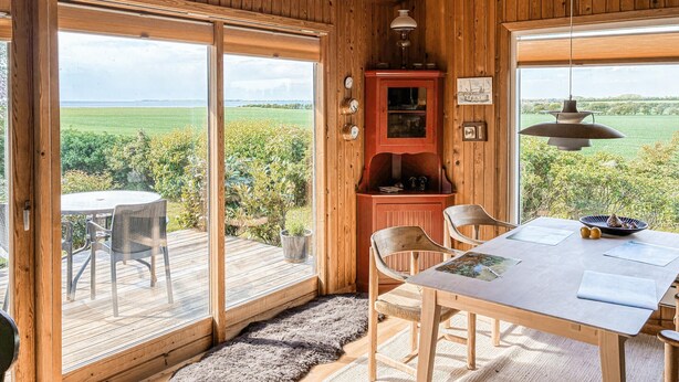 A wooden interior with a table, chairs, a cabinet, and large windows offering a view of greenery. - Gorgeous home in Slagelse with house sea view (Slagelse)