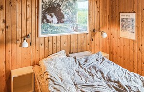 A wooden-paneled room with a bed, a window with a view of greenery, a framed painting, and a desk lamp. - Gorgeous home in Slagelse with house sea view (Slagelse)