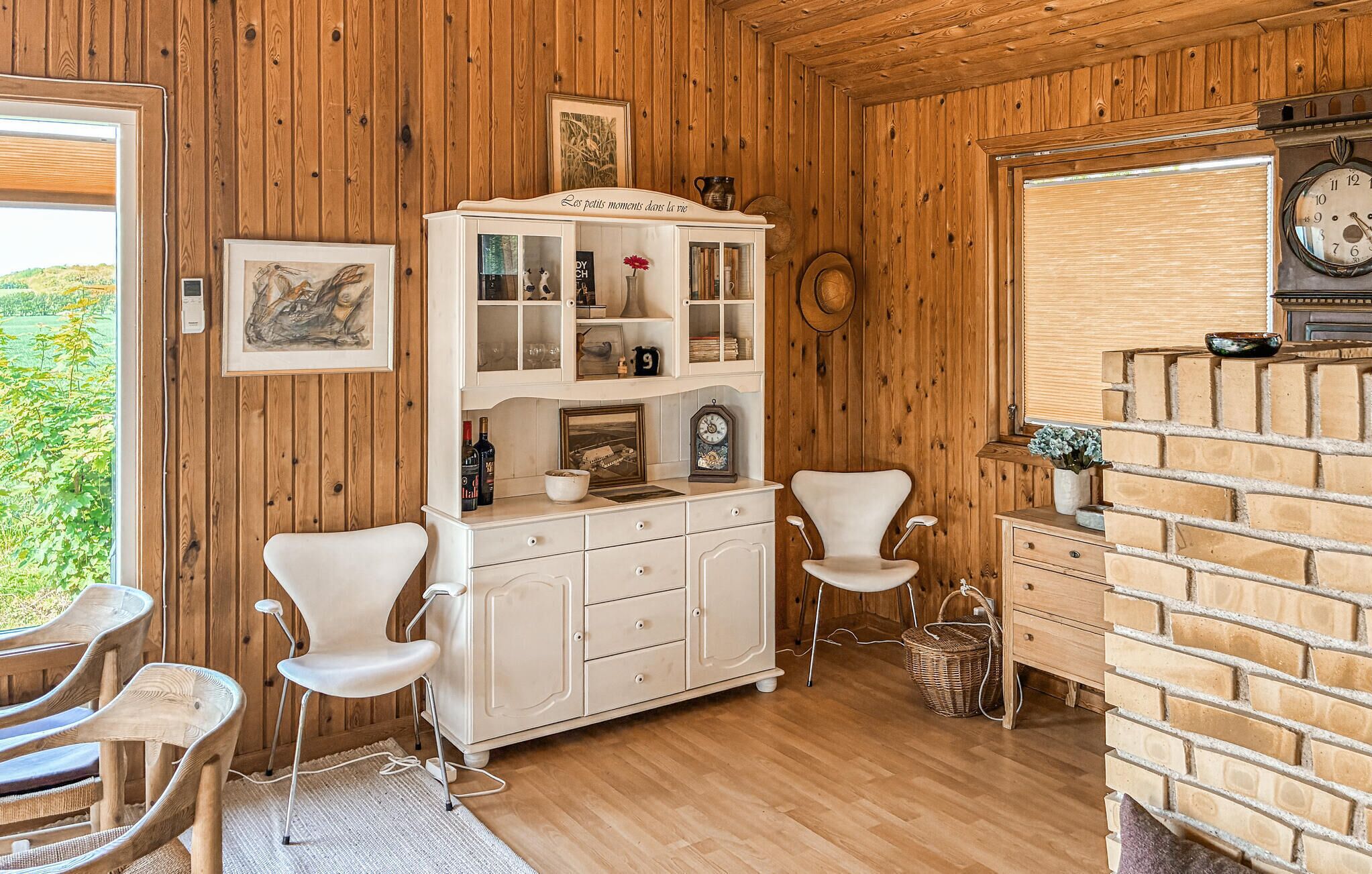A wooden-paneled room with a white cabinet, two white chairs, a wicker basket, and a brick wall.