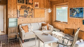 A cozy room with a sofa, a small table, a chair, and wooden walls adorned with artwork. - Gorgeous home in Slagelse with house sea view (Slagelse)