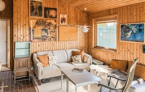 A cozy room with a sofa, a small table, a chair, and wooden walls adorned with artwork. - Gorgeous home in Slagelse with house sea view (Slagelse)
