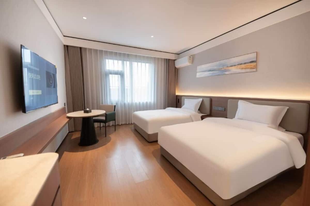 A hotel room with a bed, bedside tables, a TV, a window with curtains, and a painting on the wall.