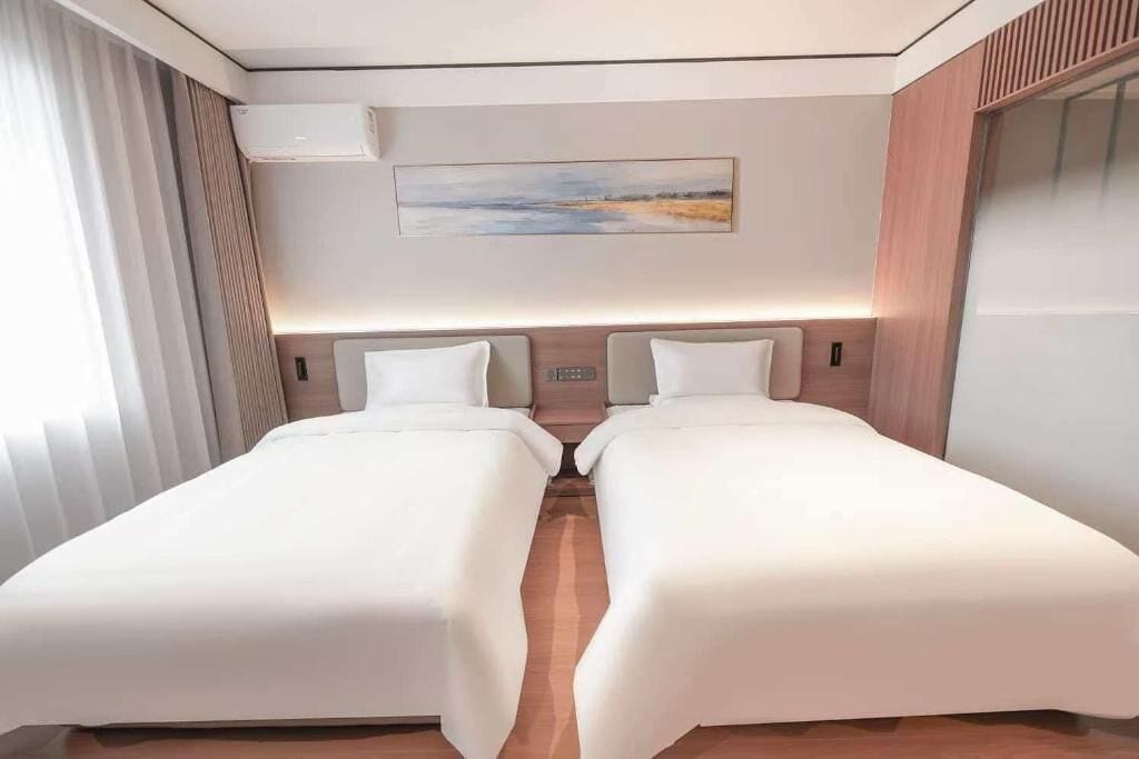 A hotel room with two beds, a painting on the wall, and an air conditioning unit.