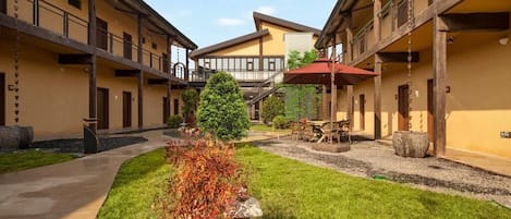 A courtyard with a central pathway, a small tree, and a seating area with a table and chairs.