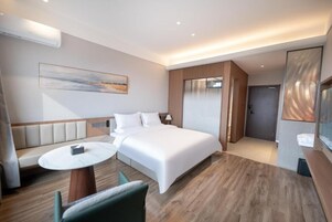 Una habitación de hotel moderna con una cama grande, un área de descanso con mesa y vistas a la ciudad.