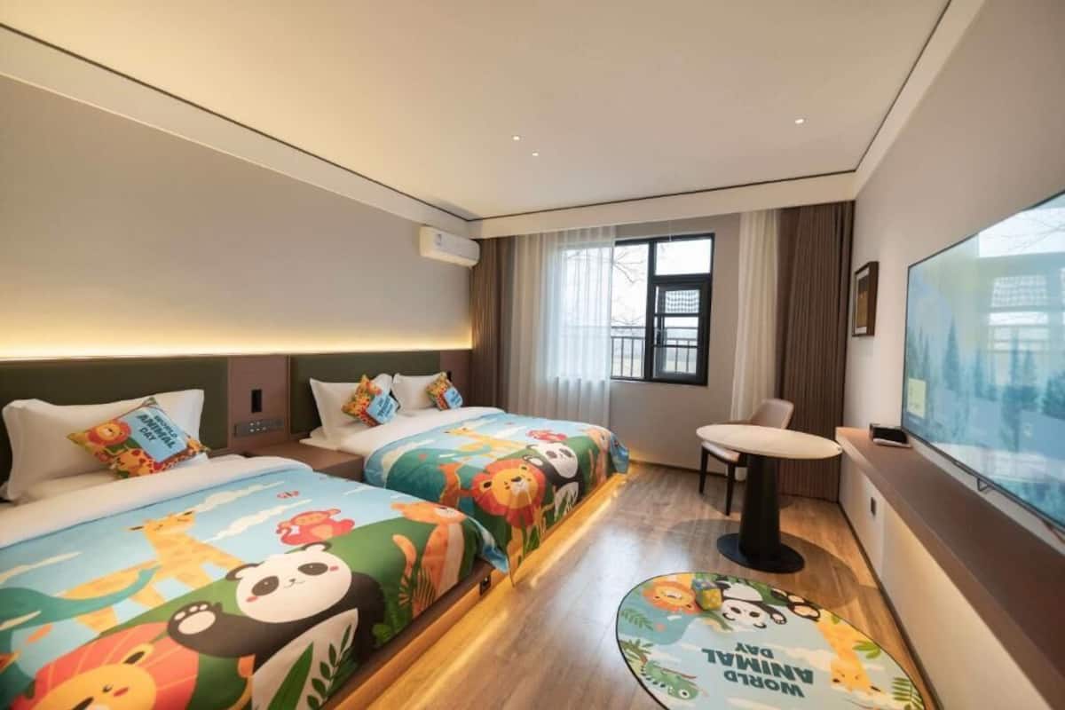 A hotel room with two beds, a small table, and a large window.