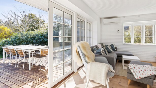 A spacious room with a large sliding glass door leading to an outdoor patio, a grey sofa, a white chair, and a small table. - 3 bedroom lovely home in Slagelse (Slagelse)