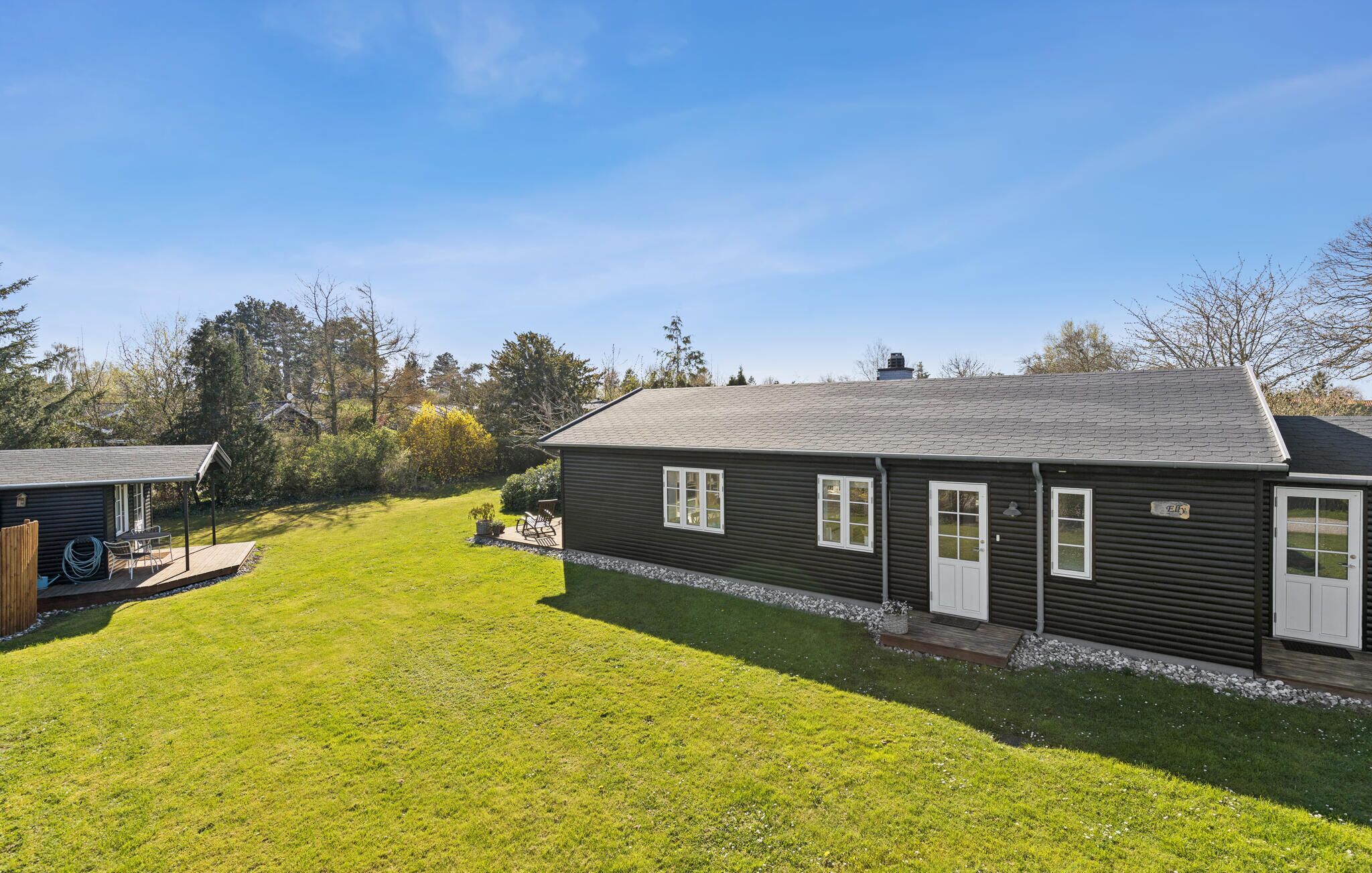 En enplansbyggnad med en mörk fasad, en huvudentré och en liten veranda med utomhusmöbler.
