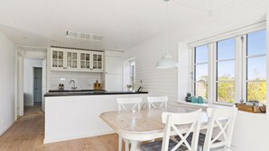 A modern kitchen with white cabinetry, a wooden dining table, and a large window with a view. - 3 bedroom lovely home in Slagelse (Slagelse)