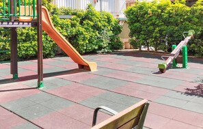 Ein Spielplatz mit Rutsche und Schaukeln, umgeben von viel Grün.