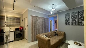A compact living space with a kitchenette, a sofa, a patterned rug, and abstract wall art. - El Pantheon Guest House and Apartments (Cape Town)