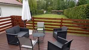 Eine Holzterrasse mit Korbmöbeln, einem runden Tisch und einem weißen Sonnenschirm.