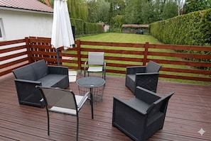 Une terrasse en bois avec des meubles en osier, une table ronde et un parasol blanc.