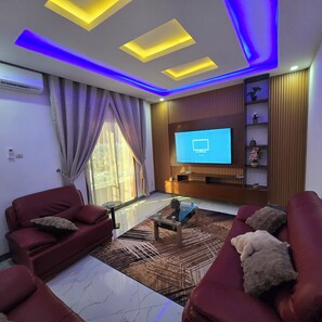 A modern living room with a flat-screen TV, red sofas, a glass coffee table, and a patterned rug. - 3BEDROOMS APPART VIP (Dakar)
