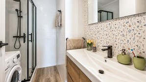 A bathroom with a shower, a washing machine, a sink with a mirror, and a floral-patterned wall. - 2 bedroom beach front apartment in Torrevieja (Torrevieja)