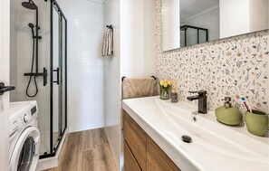 Ein Badezimmer mit Dusche, Waschmaschine, Waschbecken mit Spiegel und einer Wand mit Blumenmuster.