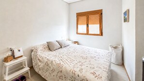 A bedroom with a bed, a bedside table, a lamp, a window with blinds, and a ceiling light. - 2 bedroom beach front apartment in Torrevieja (Torrevieja)