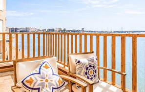 Ein Balkon mit Holzwerteln, zwei gepolsterten Stühlen und Blick auf einen Yachthafen und Stadtpanorama.