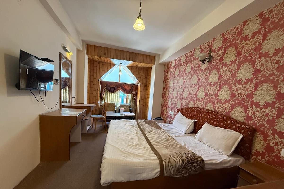 Una habitación de hotel con cama, escritorio, silla, televisor y ventana con cortinas.