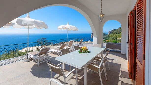 Eine Terrasse mit Tisch und Stühlen, einer Blumenkomposition und Meerblick.